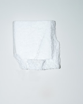A white, irregularly shaped block of polystyrene foam is positioned centrally against a plain, light background. The texture of the foam is visible, showcasing its porous and slightly rugged surface.