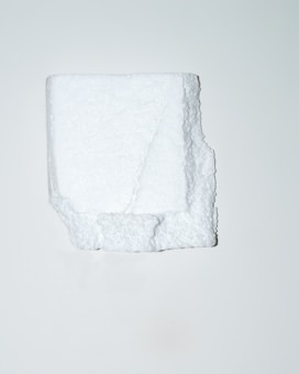 A white, irregularly shaped block of polystyrene foam is positioned centrally against a plain, light background. The texture of the foam is visible, showcasing its porous and slightly rugged surface.