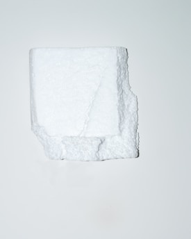 A white, irregularly shaped block of polystyrene foam is positioned centrally against a plain, light background. The texture of the foam is visible, showcasing its porous and slightly rugged surface.
