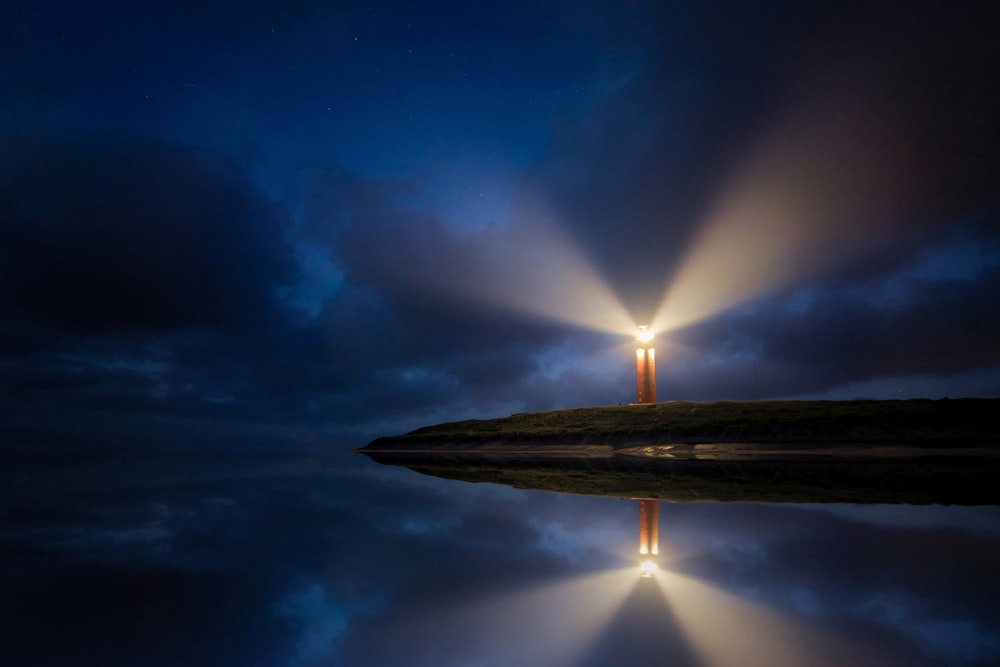 lighted brown lighthouse beside body of water