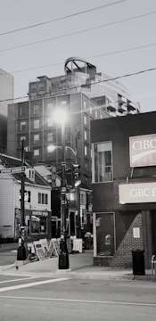 A street scene features a mix of modern and older buildings, including a high-rise with unique architectural elements. There are streetlights, multiple storefronts with signage, and a visible street sign for Spring Garden Road. Sidewalk advertising boards add to the urban atmosphere.