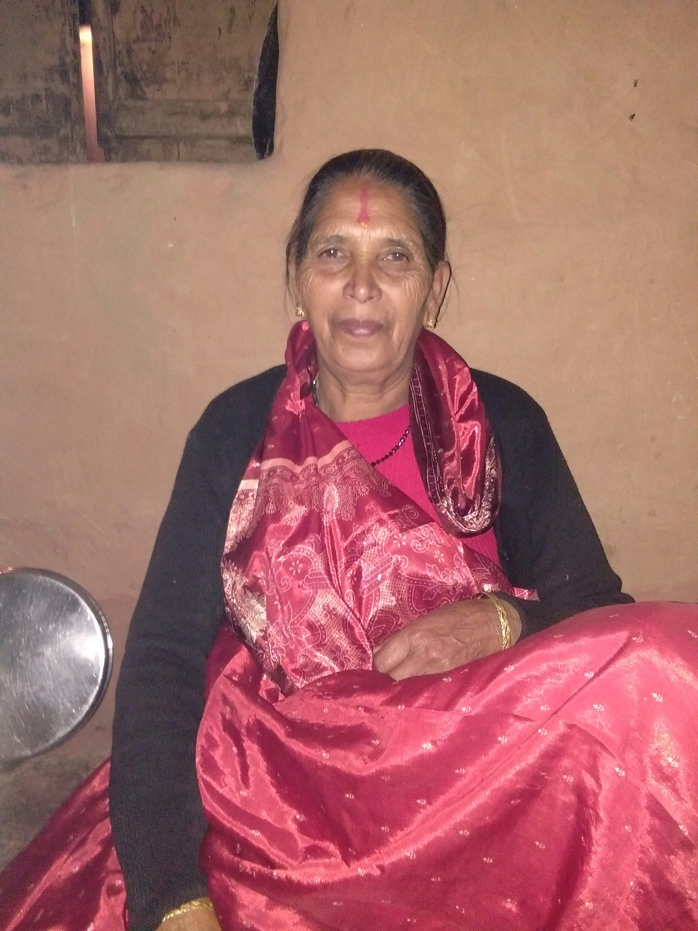 Older Indian woman with warm smile, rural village background, traditional attire