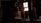 A dimly lit attic space with wooden beams and a partially visible roof letting in natural light through a small window. A person is sitting on a wooden surface, silhouetted against the light.