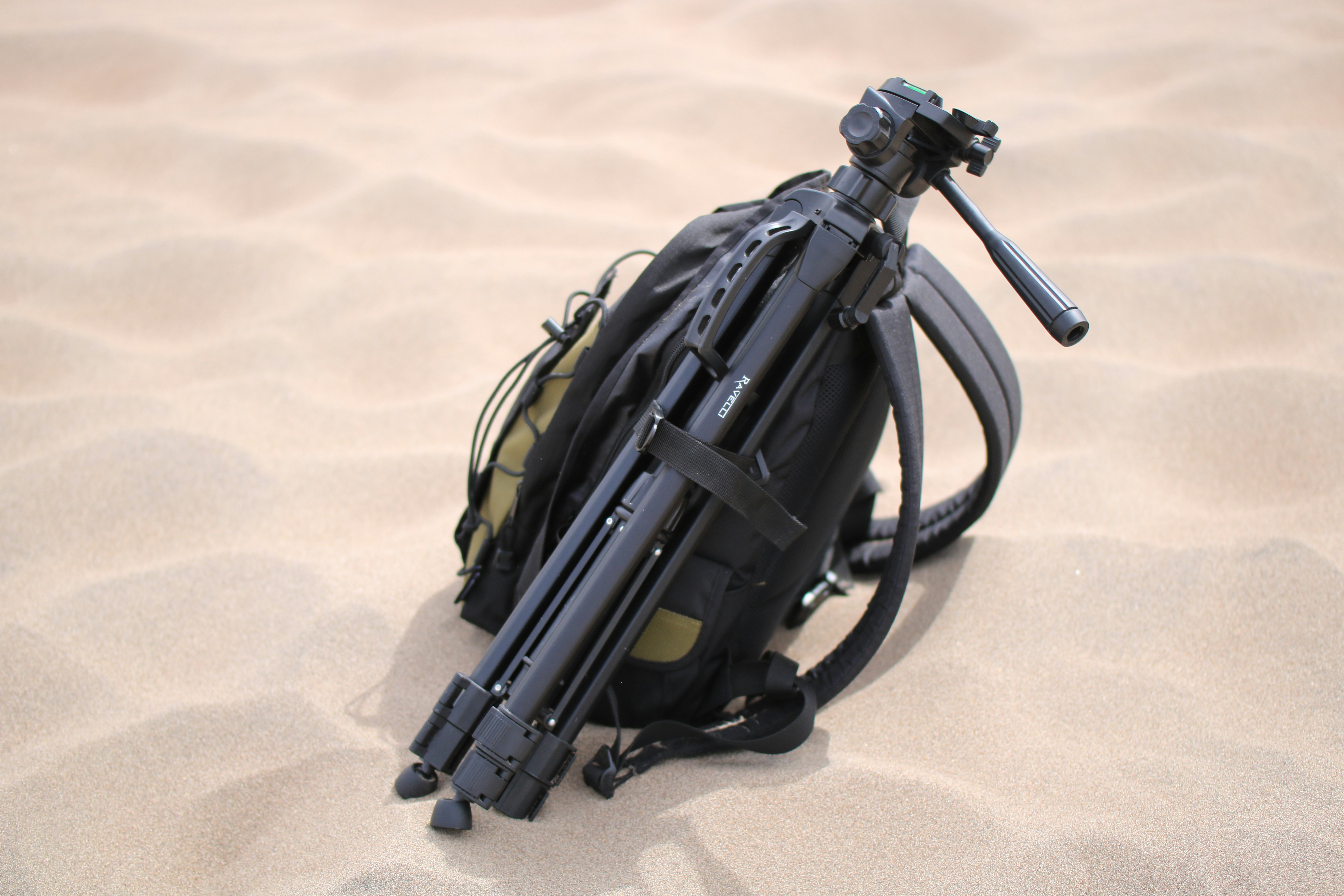 black tripod and yellow backpack on sand