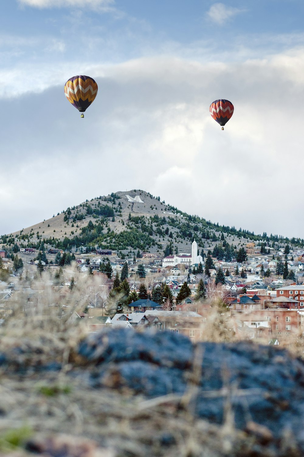 昼間、山の近くで空中に浮かぶ2つの色とりどりの熱気球