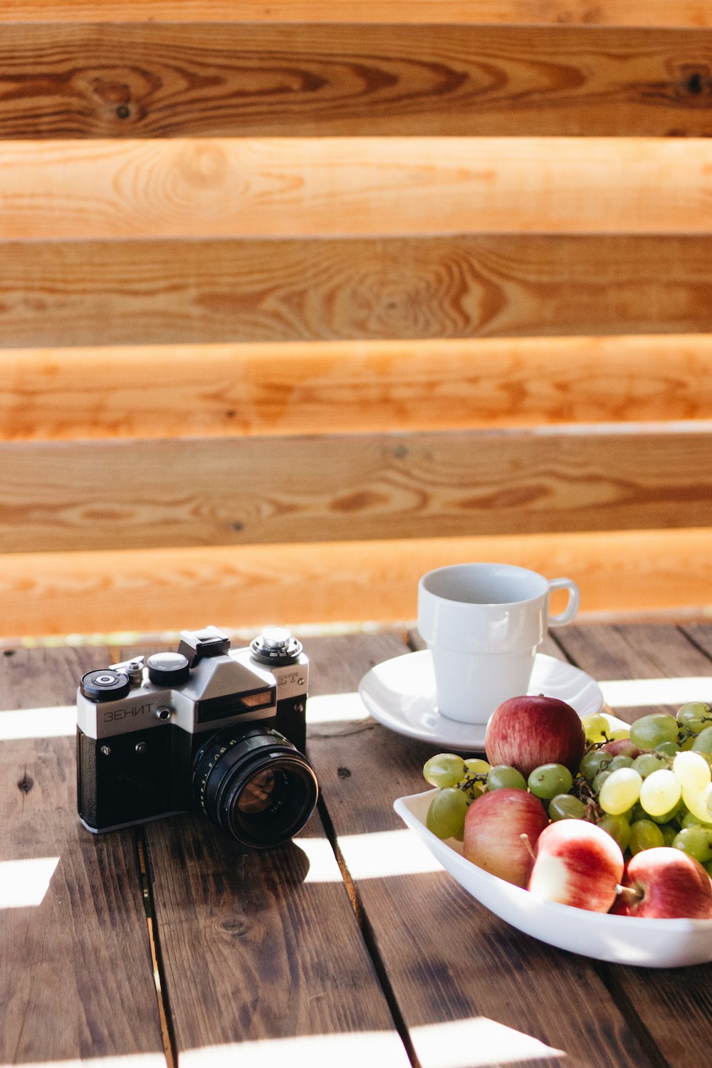 macchina fotografica IMC nera e grigia accanto alla tazza bianca sul piattino e frutta nella ciotola