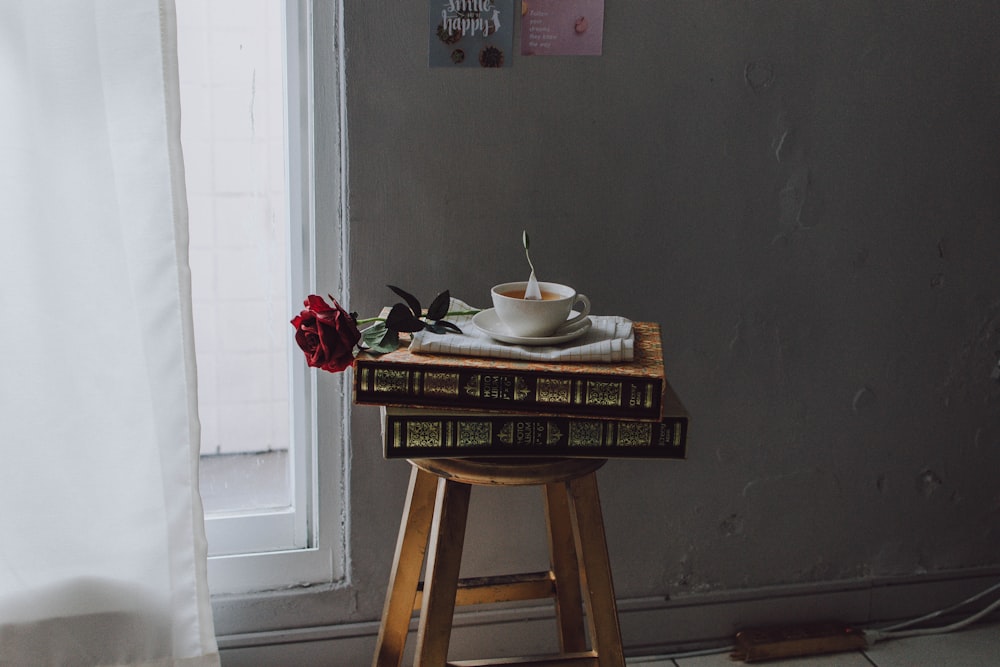 white ceramic teacup on saucer plate on books on stool near window at room