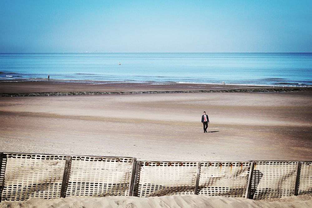 man walking at the coastline near white fences