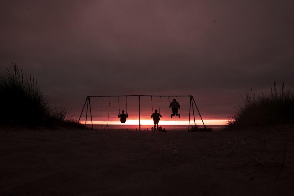 silhouette of three person swinging on outdoor swing