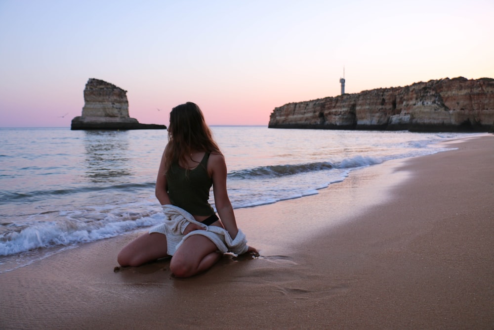 femme portant un débardeur noir assise sur du sable gris près de la plage