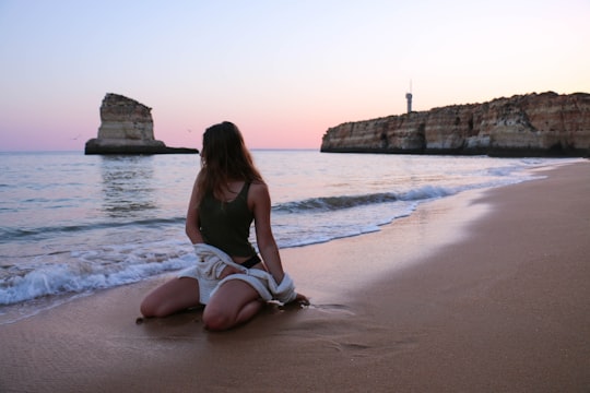 woman wearing black tank top sitting on gray sand near beach in Faro Portugal