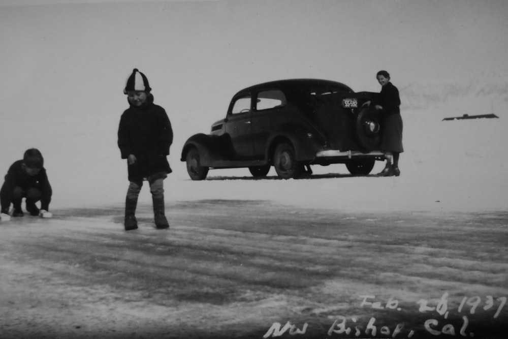 grayscale photo of two boys near vintage black car