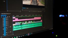 A computer screen displays a video editing software interface with multiple tracks visible in the timeline. The timeline includes video and audio tracks, colored in pink, green, and blue, indicating different layers or elements. The software has various tools and menus around the timeline.