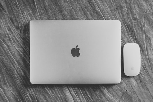 A laptop and a mouse with a sleek, minimalist design placed on a wooden surface. The laptop has a metallic finish with a distinct logo in the center. The mouse is positioned next to the laptop, both sharing a similar aesthetic.