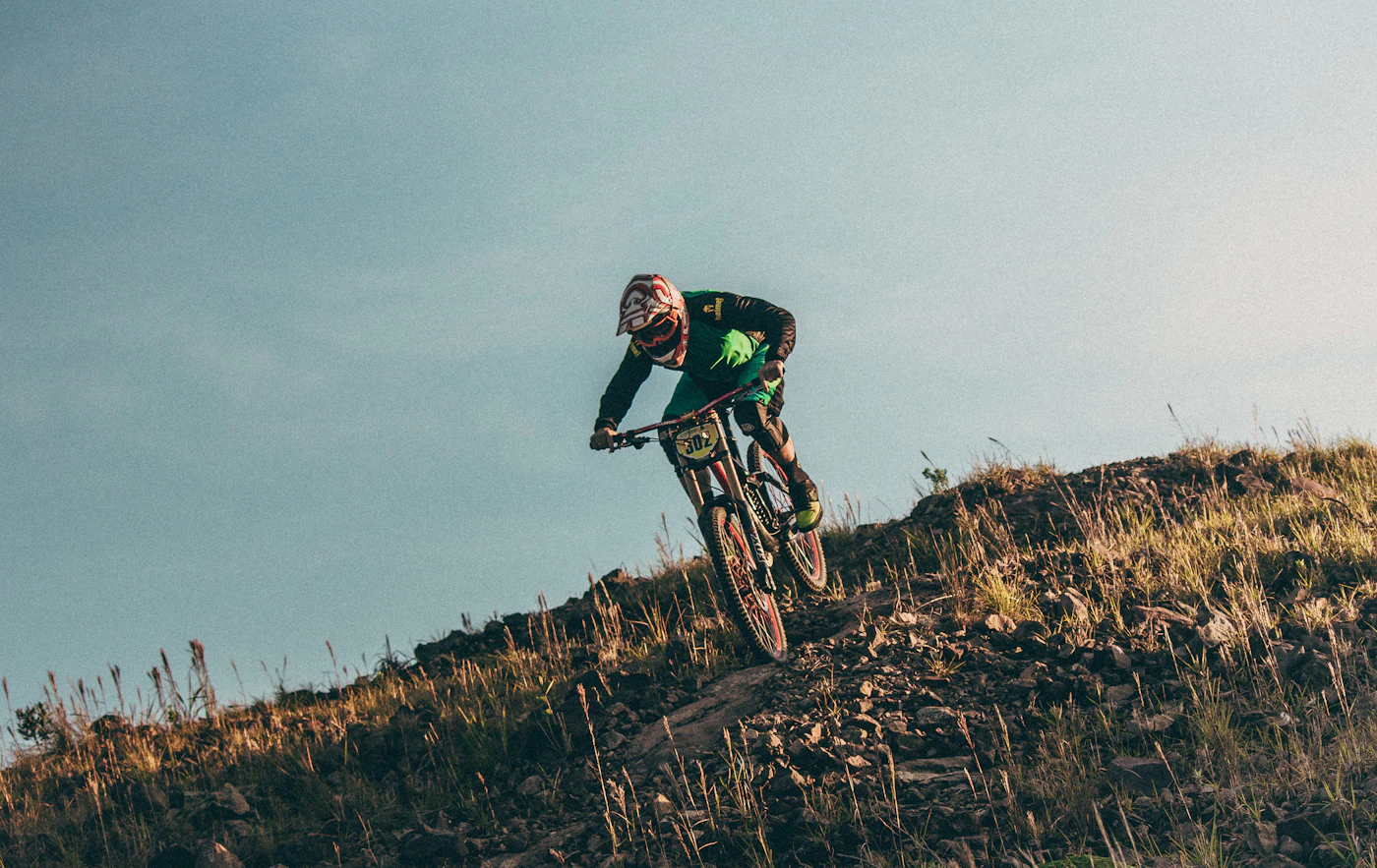 Mountain biker descending a rocky hillside trail in golden evening light