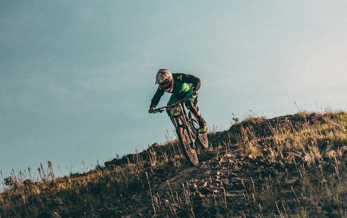 Pilote de VTT en descente sur une crête herbeuse, casque intégral, lumière de fin de journée