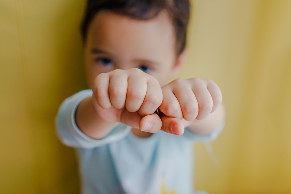 toddler boy wearing white shirt leaning back on brown wooden wall