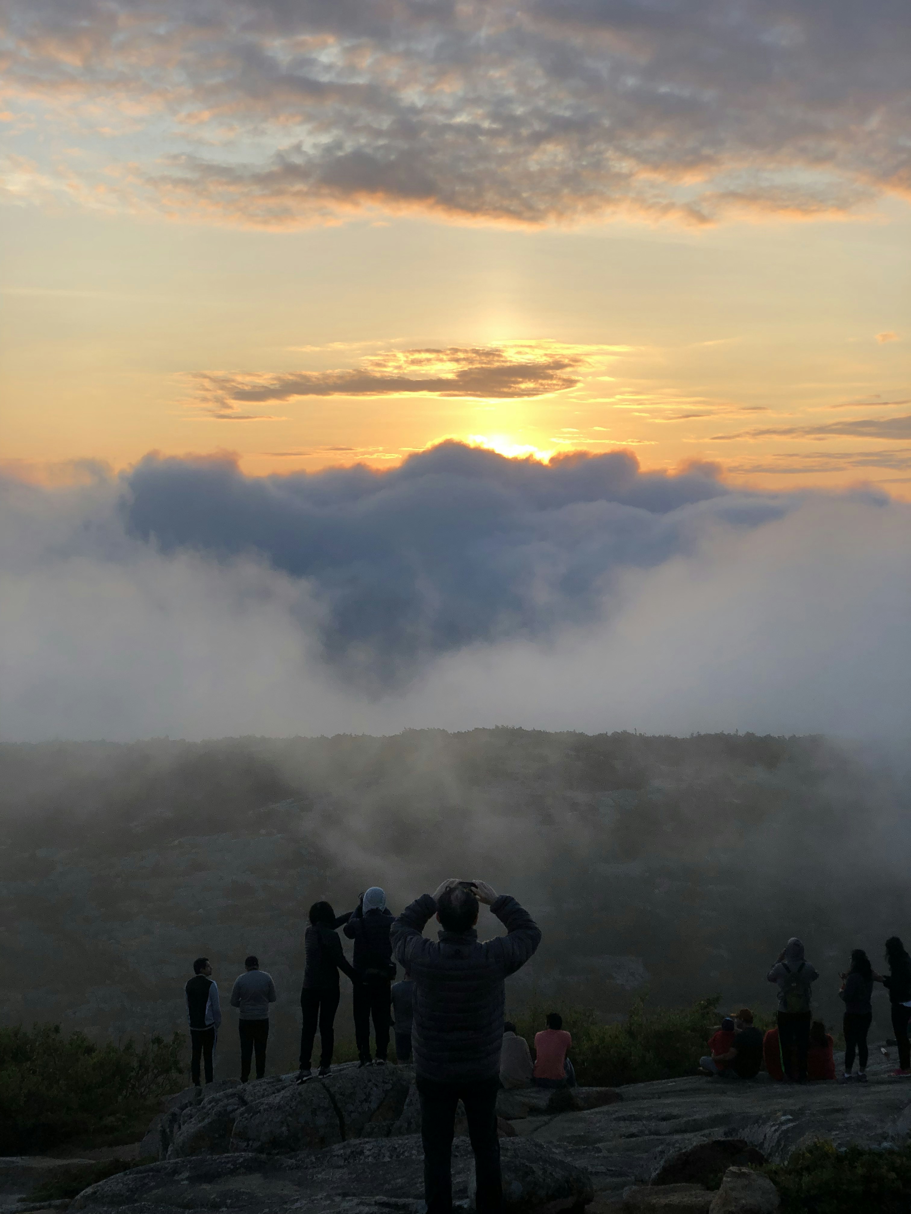Hikers stand on a mountain peak looking over misty clouds.