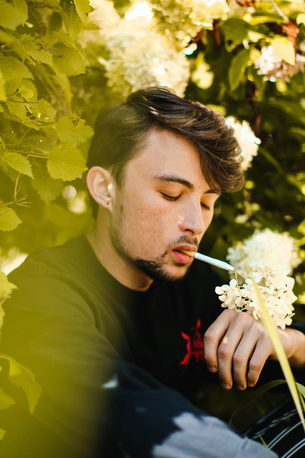 hombre fumando cigarrillo cerca de flores blancas