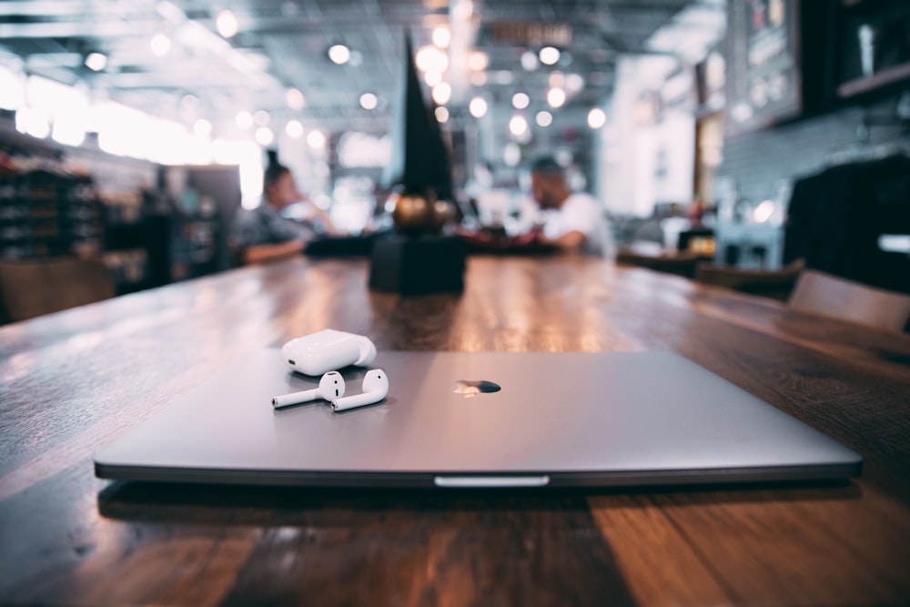 fotografia de foco seletivo de AirPods brancos com estojo de carregamento no MacBook prateado na mesa