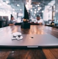 selective focus photography of white AirPods with charging case on silver MacBook on table