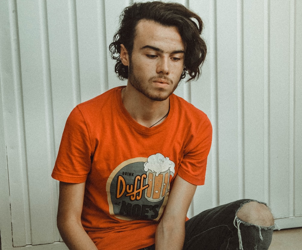 man wearing orange crew-neck t-shirt near white wall