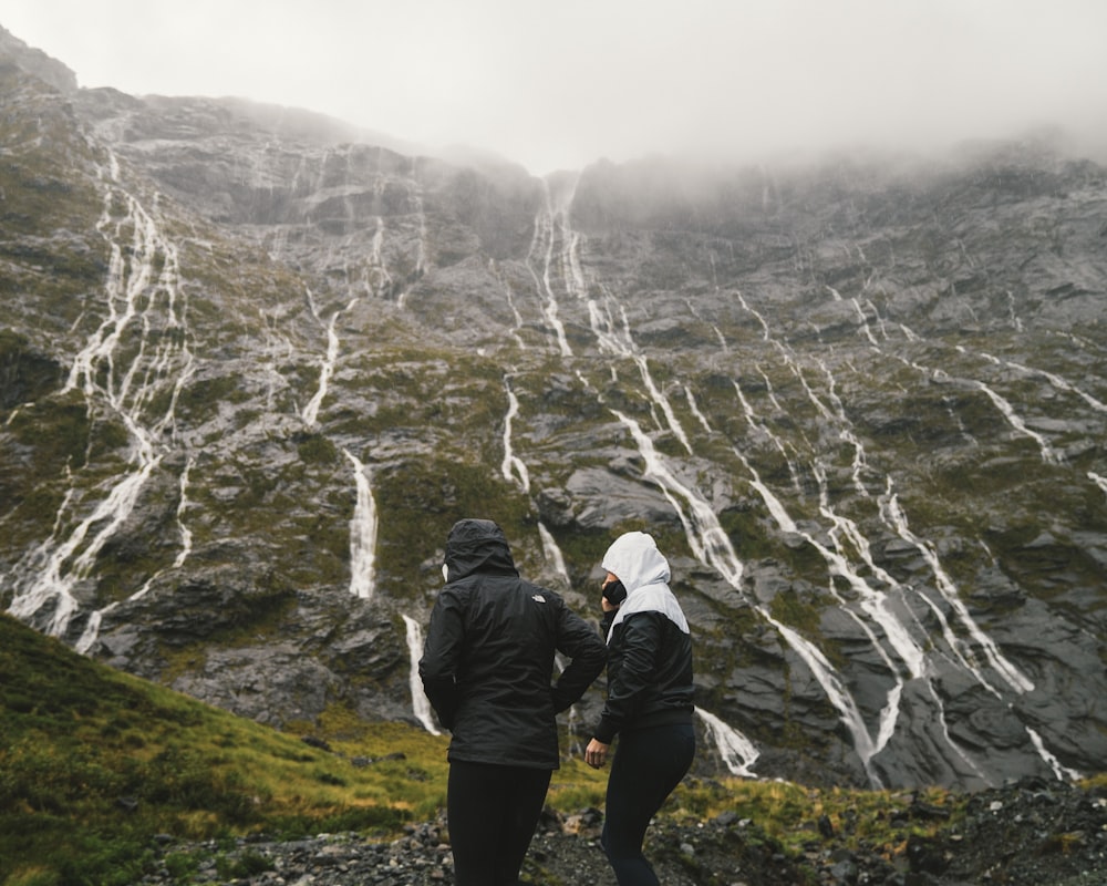 two people standing near high-rise mountain over cloudy sky at daytime