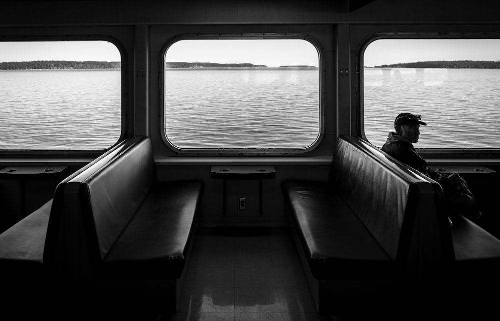 man sitting on watercraft bench grayscale photo