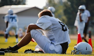 selective focus photography of man sitting on field wearing football gear