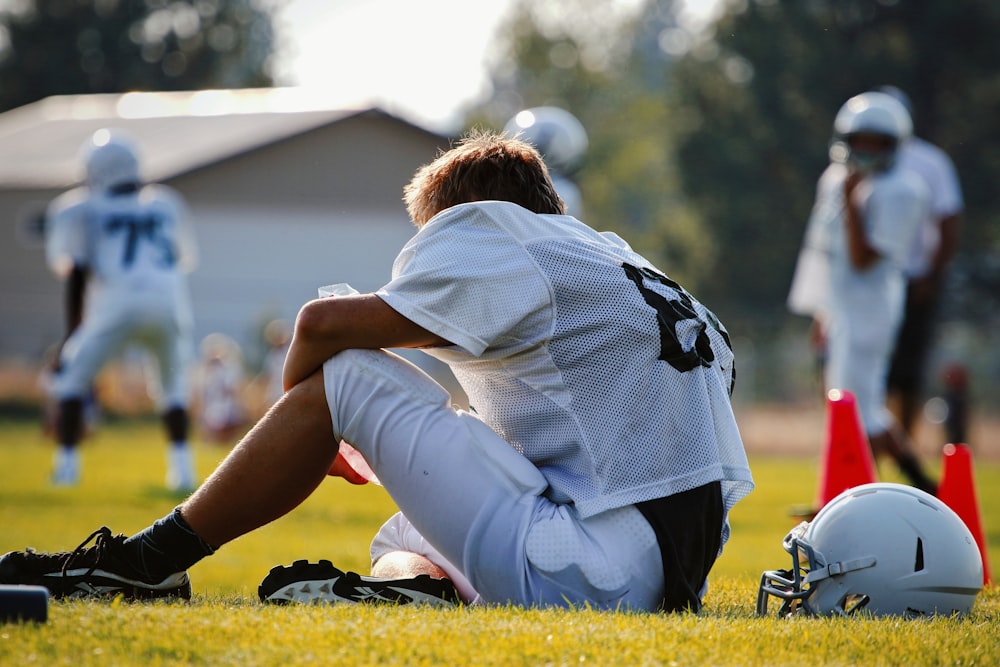 selective focus photography of man sitting on field wearing football gear