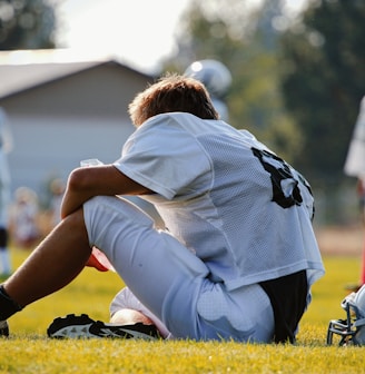 selective focus photography of man sitting on field wearing football gear