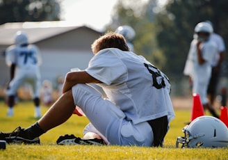 selective focus photography of man sitting on field wearing football gear