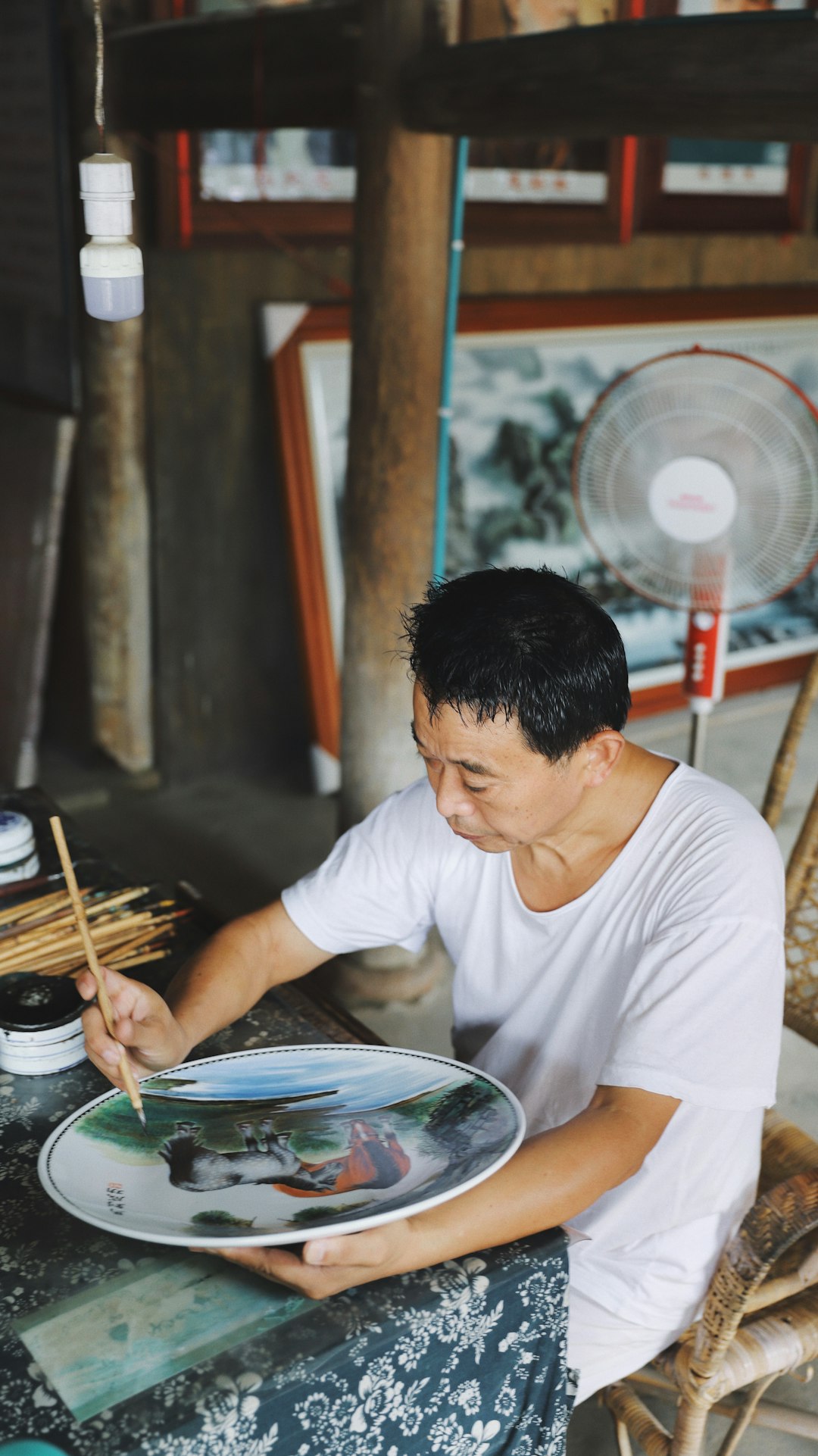 man sitting on chair while painting on plate
