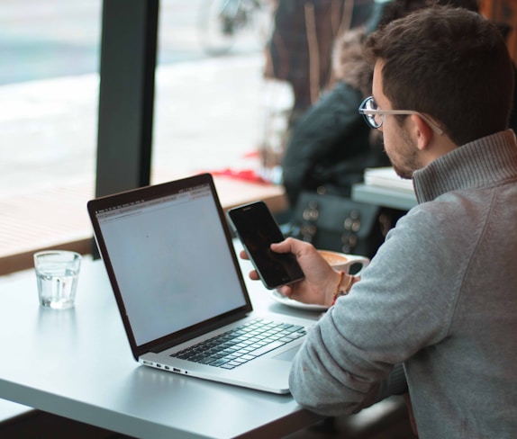 man sitting near table with laptop and smartphone near window