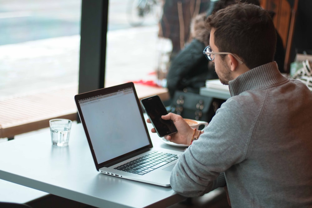 Mann sitzt in der Nähe des Tisches mit Laptop und Smartphone in der Nähe des Fensters