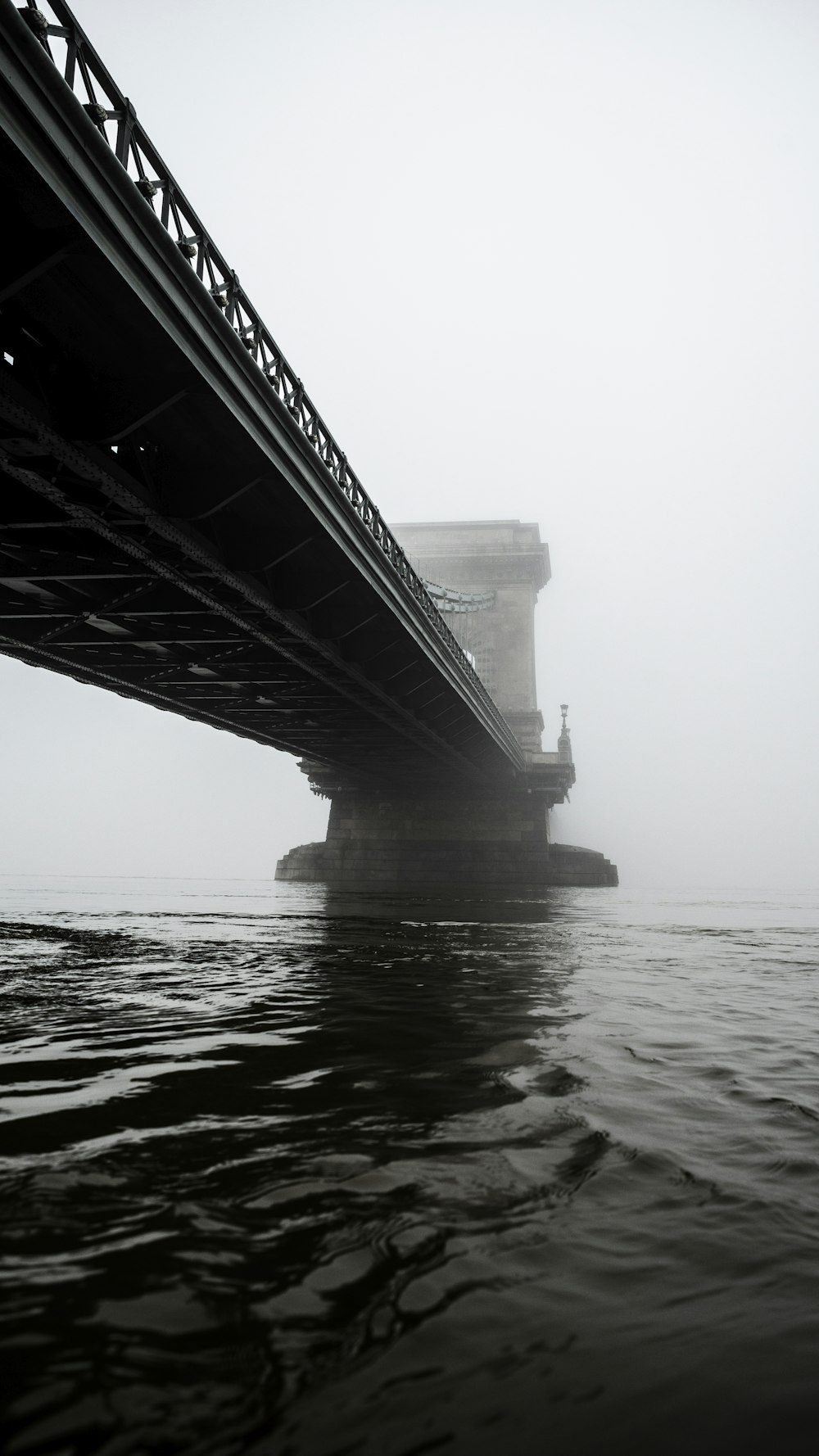 Fotografía en escala de grises de un puente colgante sobre aguas tranquilas