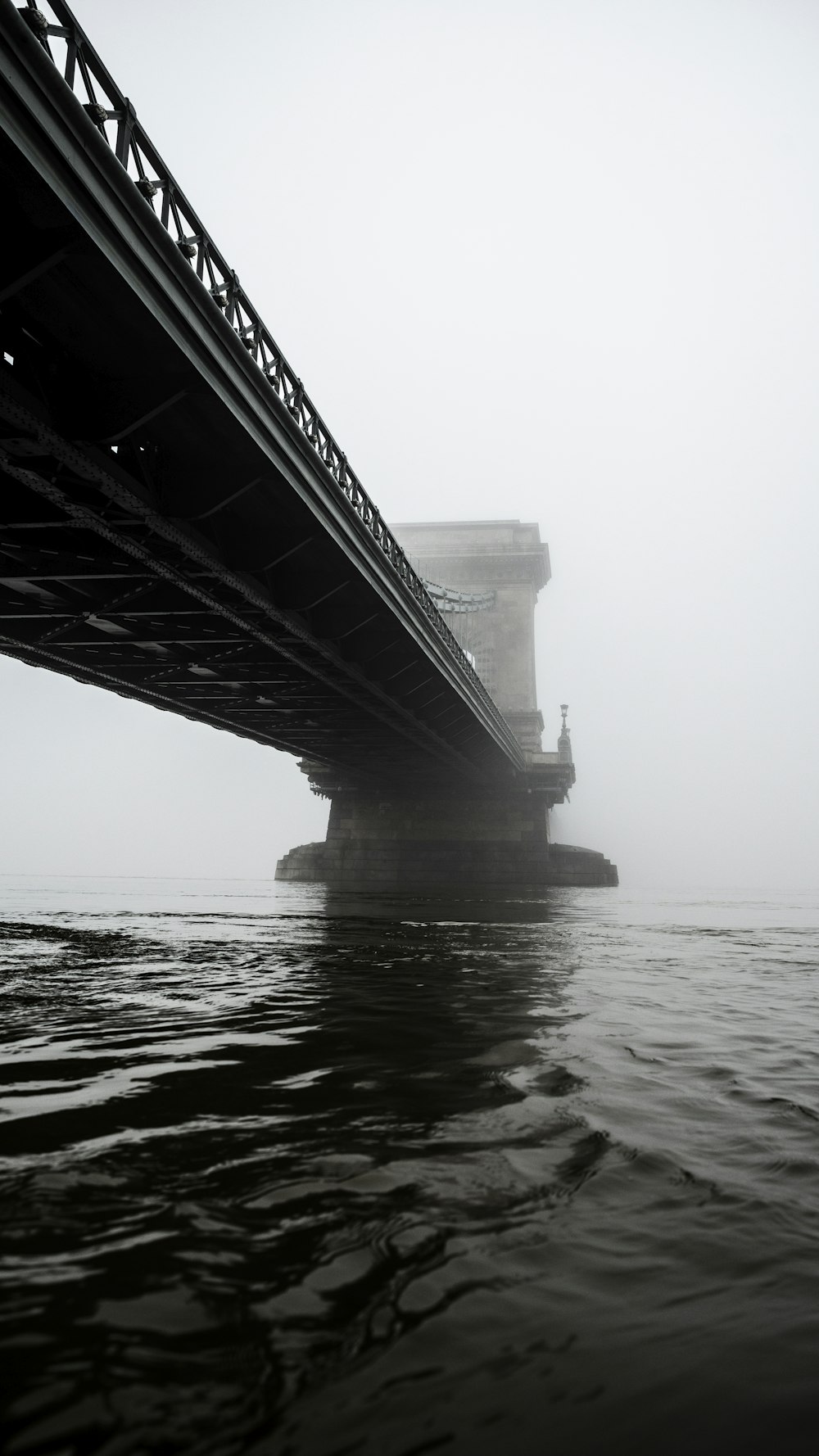 grayscale photography of suspension bridge across calm water