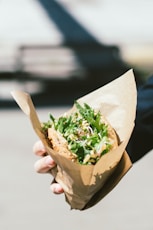 person holding brown paper bag with vegetable sandwich