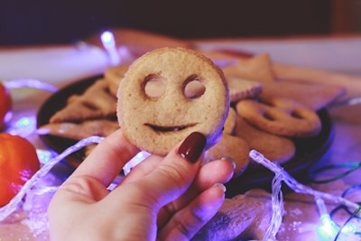A hand holding a perfectly decorated sugar cookie shaped like a smiling face.