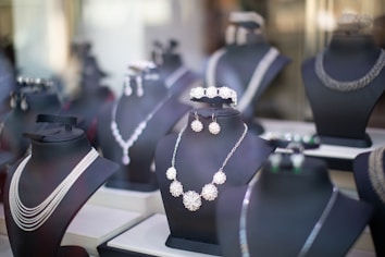 A collection of elegant jewelry sets displayed on black mannequin busts, featuring necklaces, earrings, and bracelets with intricate designs and sparkling details, set in a well-lit store window.