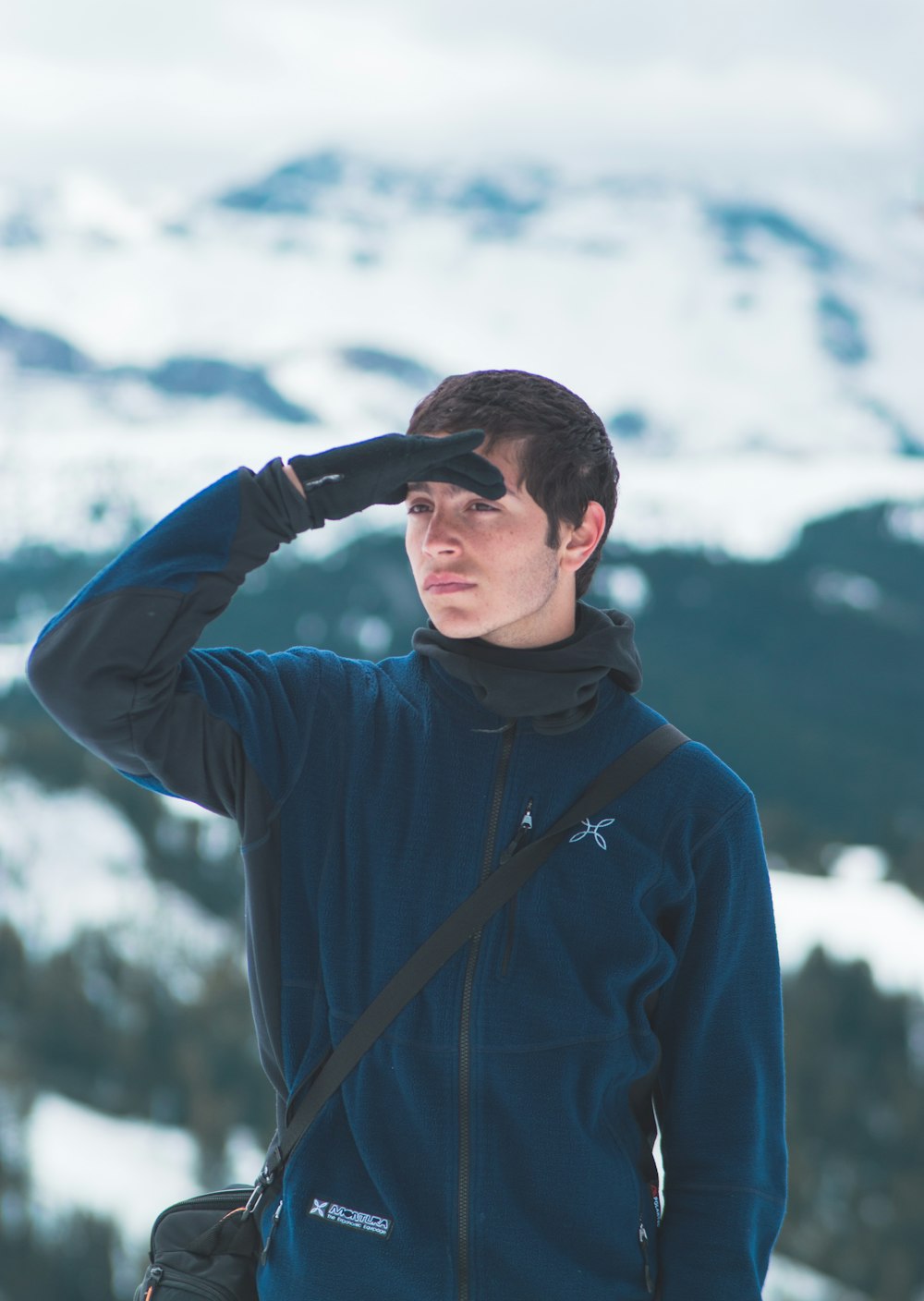 selective focus photography of man's right hand on forehead standing on snow capped mountain during daytime