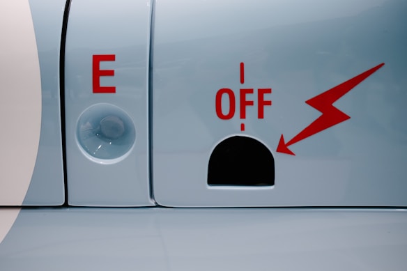A metallic surface features a prominent red letter 'E' alongside a clear circular object. Nearby, bold red text reads 'OFF' with a red lightning bolt design pointing towards a black semicircular cutout.