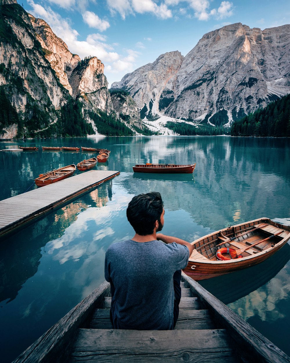 갈색 나무 계단에 앉아 낮에 산 근처의 호수를 응시하는 남자