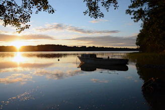 A small private boat anchored near a peaceful lakeside with a family enjoying the view at sunset.