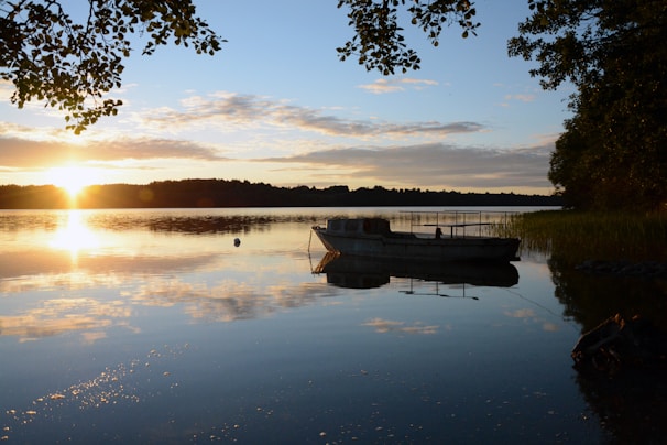 A serene sunset over a calm lake with a luxury boat anchored.