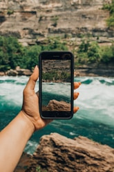 person holding black smartphone focusing body of water