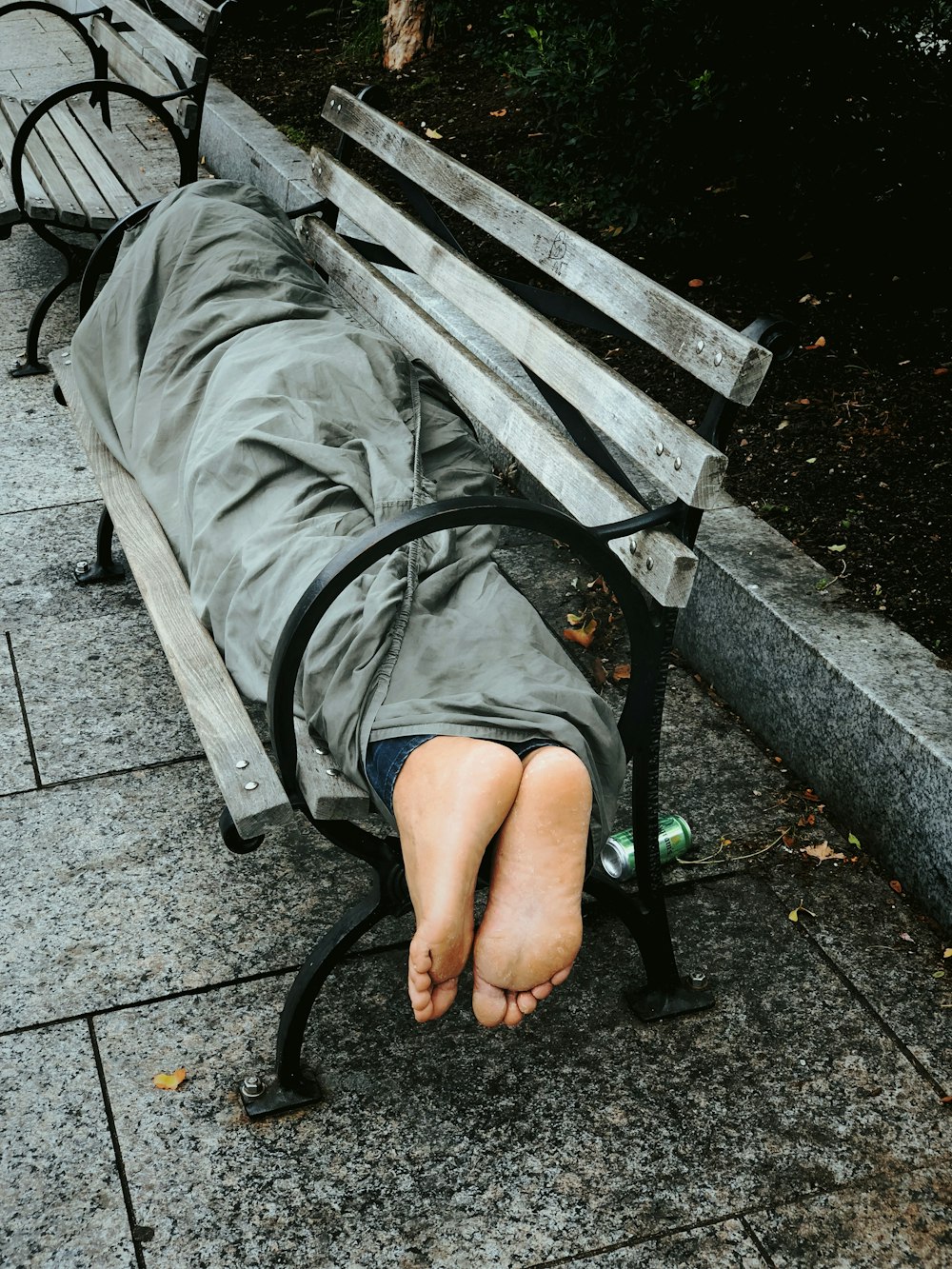 persona che dorme su una panchina coperta da una coperta grigia