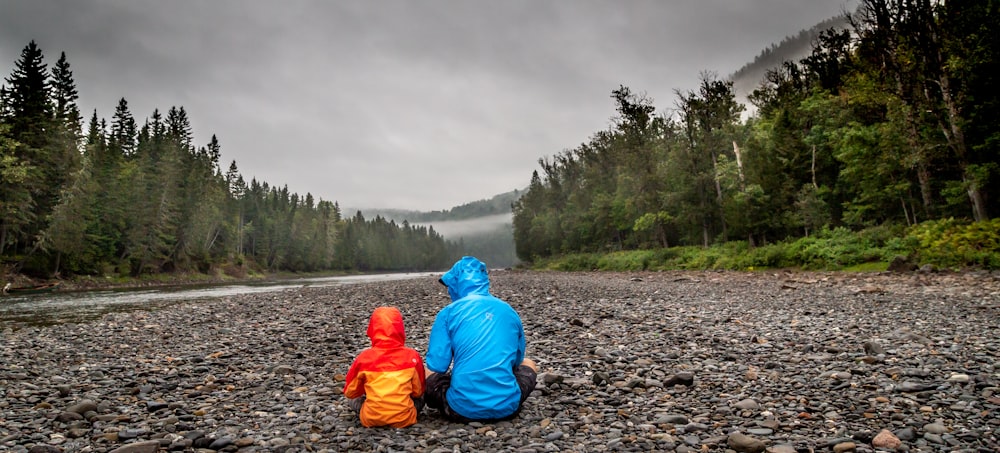 two persons sitting beside body of water