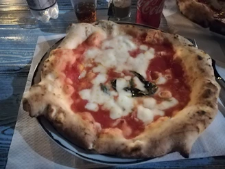 A cozy restaurant table with a delicious pepperoni pizza and a cold Coca-Cola bottle.