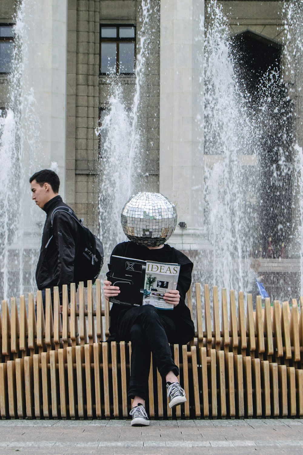 person sitting on wooden accordion bench while reading magazine at the back of water fountain